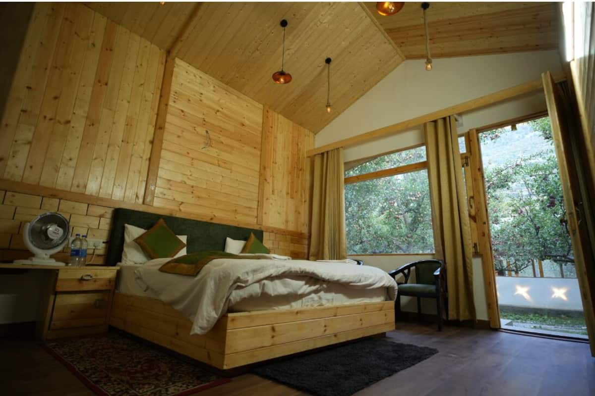 Un dormitorio de madera con cama, mesita de noche y ventana con cortinas.