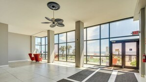 Un vestíbulo amplio con grandes ventanales, un ventilador de techo y sillas rojas.