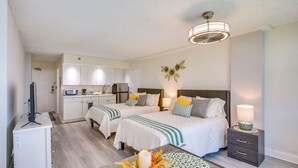 Habitación de hotel con dos camas, un escritorio, una silla, una lámpara y un ventilador de techo.