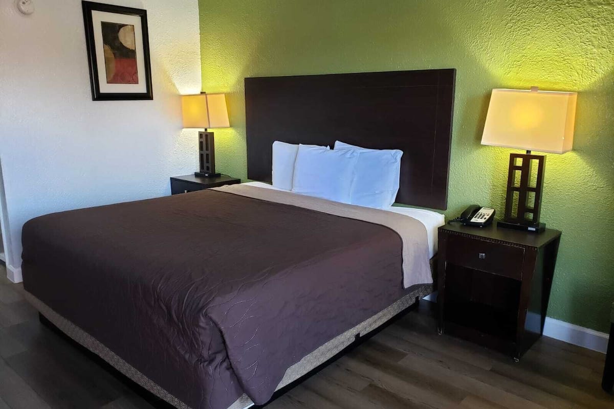 A hotel room with a large bed, two bedside tables, a nightstand, a framed picture on the wall, and a green textured wall.
