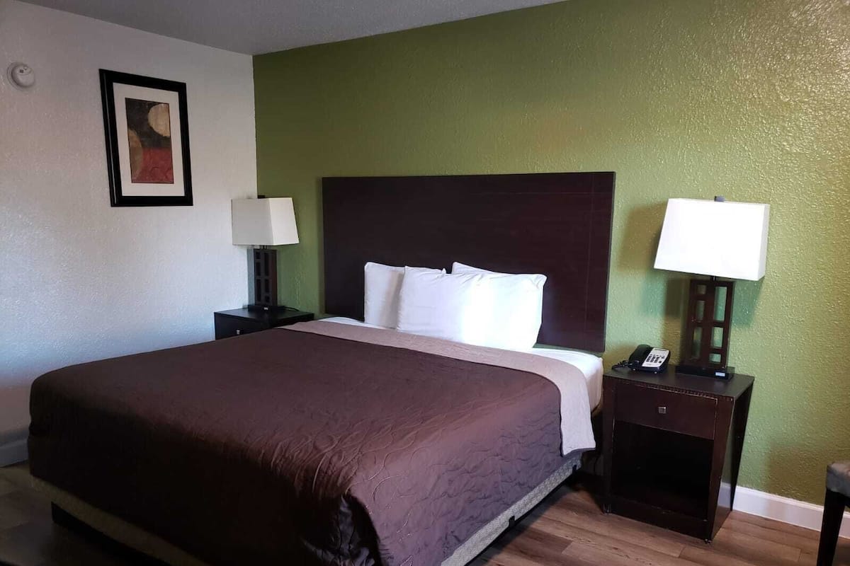 A hotel room with a large bed, two bedside tables with lamps, a framed picture on the wall, and a green accent wall.