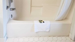 A bathtub with a shower curtain, a grab bar, and a towel. - Relax Inn (Claxton)