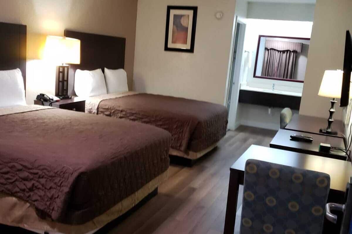 A hotel room with two beds, a desk, and a chair.