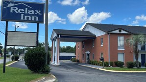 A brick building with a covered parking area and a sign for 'Relax Inn'. - Relax Inn (Claxton)
