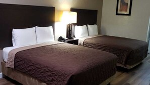 A hotel room with two beds, a nightstand with a lamp, a framed picture on the wall, and wooden flooring. - Relax Inn (Claxton)