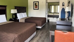 A hotel room with two beds, a desk, a chair, a mirror, and a bathroom visible through an open door.