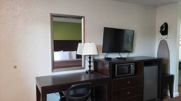A hotel room with a desk, chair, television, and a mirror.