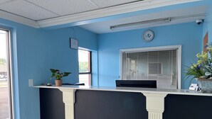 A reception desk with a clock, a window with blinds, and a potted plant. - Relax Inn (Claxton)