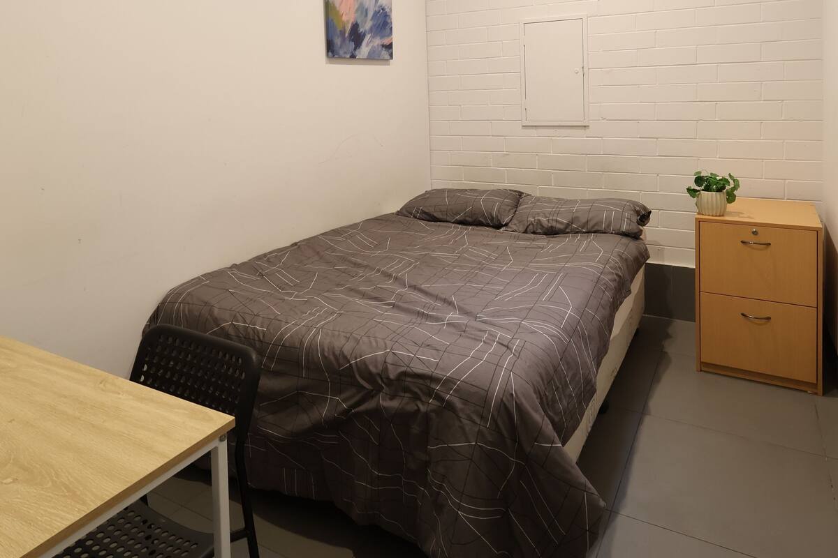 A small, modern bedroom with a bed, a desk, and a nightstand.