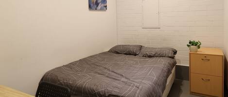 A small, modern bedroom with a bed, a desk, and a nightstand.