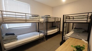 A dormitory room with bunk beds, a small table, and a window with blinds. - Quokka Backpackers Hostel Perth - note - Valid passport required to check in (WA)