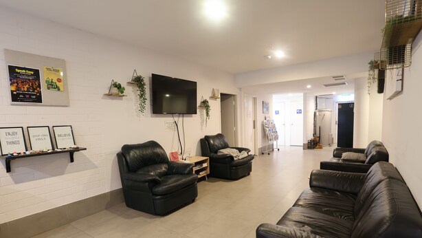 A modern living room with leather sofas, a flat-screen TV, and a wall-mounted shelf with framed pictures. - Quokka Backpackers Hostel Perth - note - Valid passport required to check in (WA)