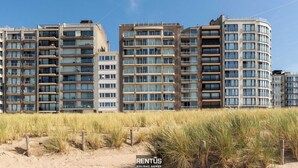 A multi-story residential building with balconies, a flat roof, and a clear sky.