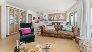 A spacious living room with a green armchair, a brown leather sofa, and a dining table set with wine glasses and a bottle.