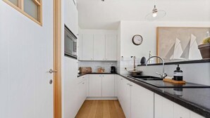 A compact kitchen with white cabinets, a wooden floor, a black countertop, and a clock on the wall.