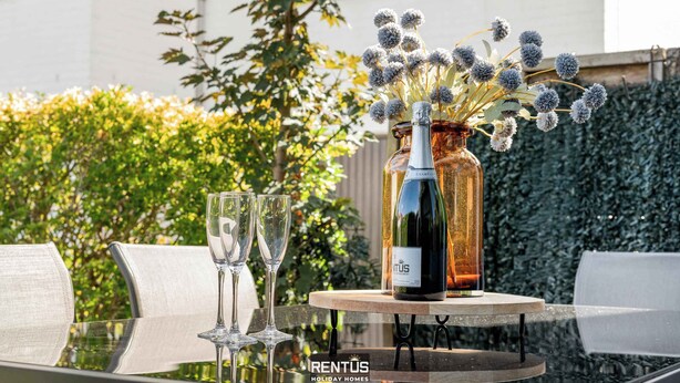 A table with two wine glasses, a bottle of wine, and a vase with flowers.