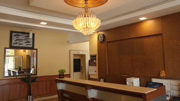 A reception area with a wooden reception desk, a large chandelier, a wall clock, and a framed picture of birds.