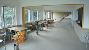 A spacious dining area with multiple tables and chairs, large windows, and a staircase leading to an upper floor.