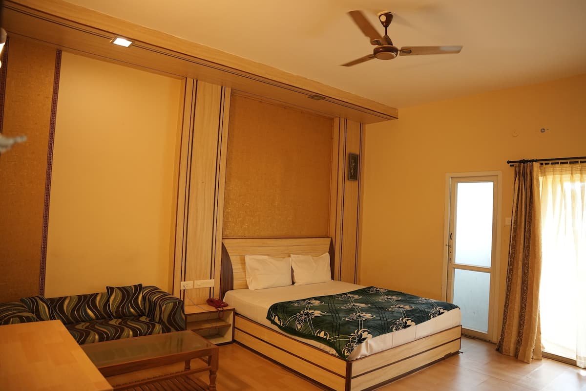 A bedroom with a bed, a sofa, a table, and a ceiling fan.