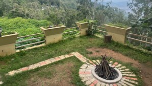 A scenic outdoor area with a fire pit, a pathway, and a railing overlooking a lush valley.