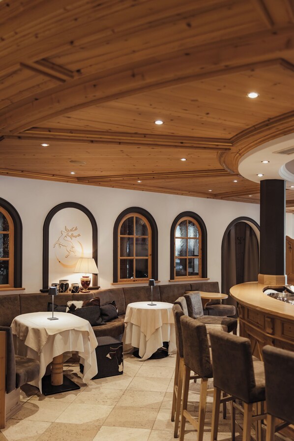 Een knus restaurantinterieur met houten balken in het plafond, gewelfde ramen en een bar.