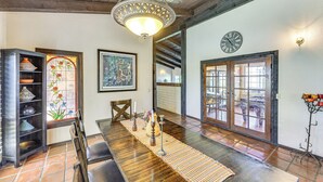 Uma sala de jantar com mesa de madeira, cadeiras, um candelabro, uma janela de vitral e um relógio na parede.