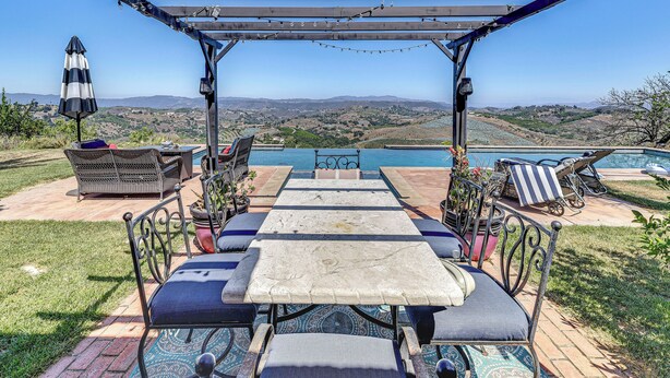 Pátio externo com pérgola, assentos e vista para piscina e paisagem.