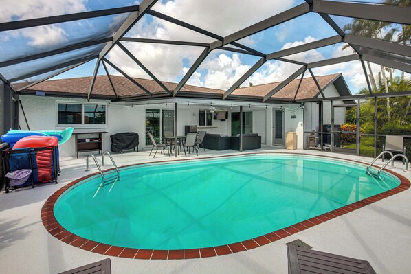 Une piscine couverte à l’eau d’un bleu cristallin, entourée d’un patio aménagé avec du mobilier d’extérieur, d’où l’on peut admirer la maison en arrière-plan.