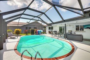 Une piscine intérieure couverte avec un toit transparent, un espace patio aménagé avec des sièges et une vue sur le jardin arrière.