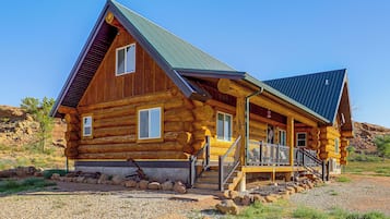 Une cabane en rondins avec un toit à forte pente, de nombreuses fenêtres et une véranda dotée d’une balustrade.