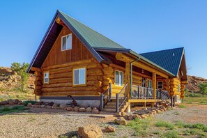 A log cabin with a steeply pitched roof, multiple windows, and a porch with a railing.