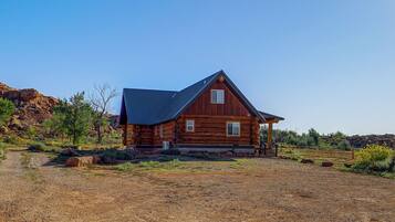 A wooden cabin with a sloped roof, situated in a dry, rocky terrain with sparse vegetation.