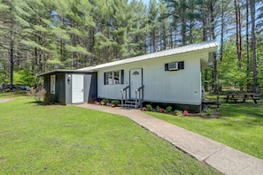 A single-story mobile home with a front porch, a small attached garage, and a picnic table in the background. - Hiking & ATV Trails On-Site: Adirondacks Abode (Greig)