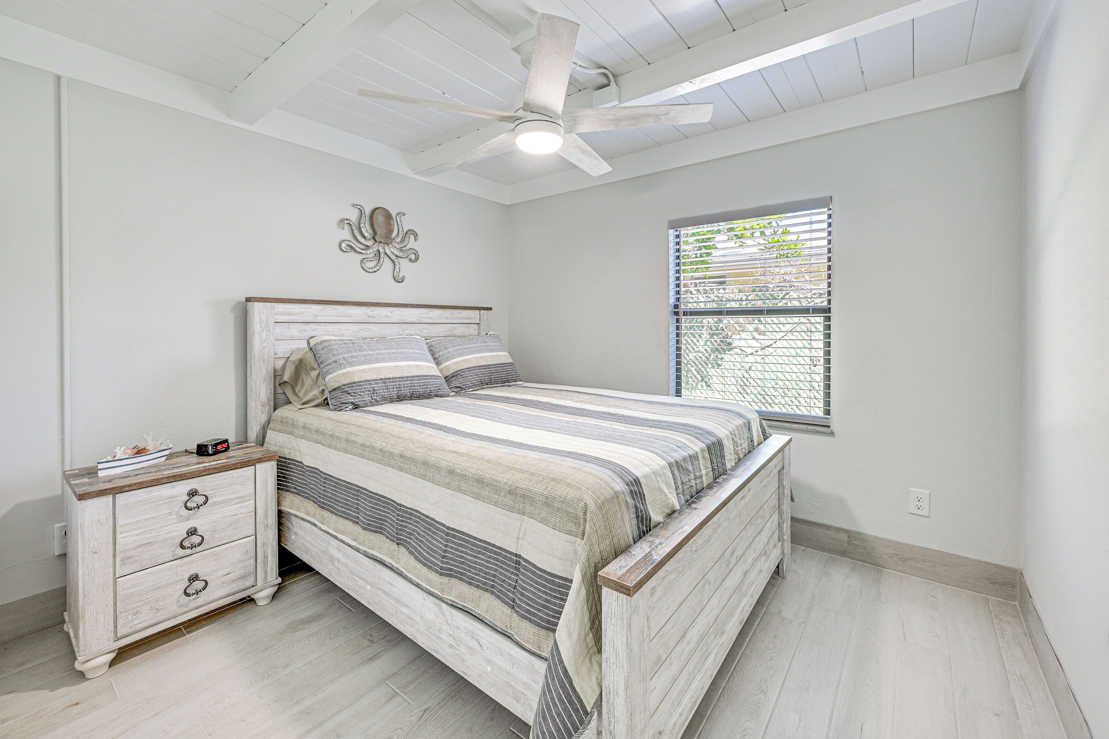 A bedroom with a bed, a nightstand, a ceiling fan, and a window with blinds.