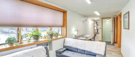 A modern hotel room with a sofa, a bedside table, and a window with blinds.
