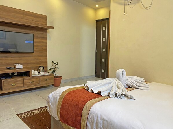 A hotel room with a bed, a TV, a wooden dresser, a potted plant, and a towel on the bed. - Hotel Tara Suites (Kathmandu)