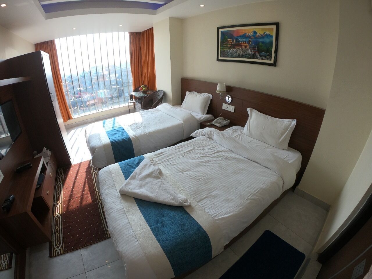A hotel room with two beds, a desk with a chair, a TV, and a window with curtains.