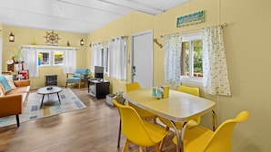 A cozy living room with a sofa, a TV, and a dining table with yellow chairs.