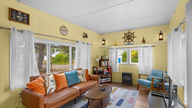 A cozy living room with a brown leather sofa, a wooden coffee table, and a blue armchair. There is a bookshelf with books and decorative items, and a television on a stand.