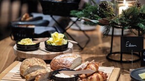 A wooden table with various breads and pastries, a candle, and a sign with the name 'Edam'.