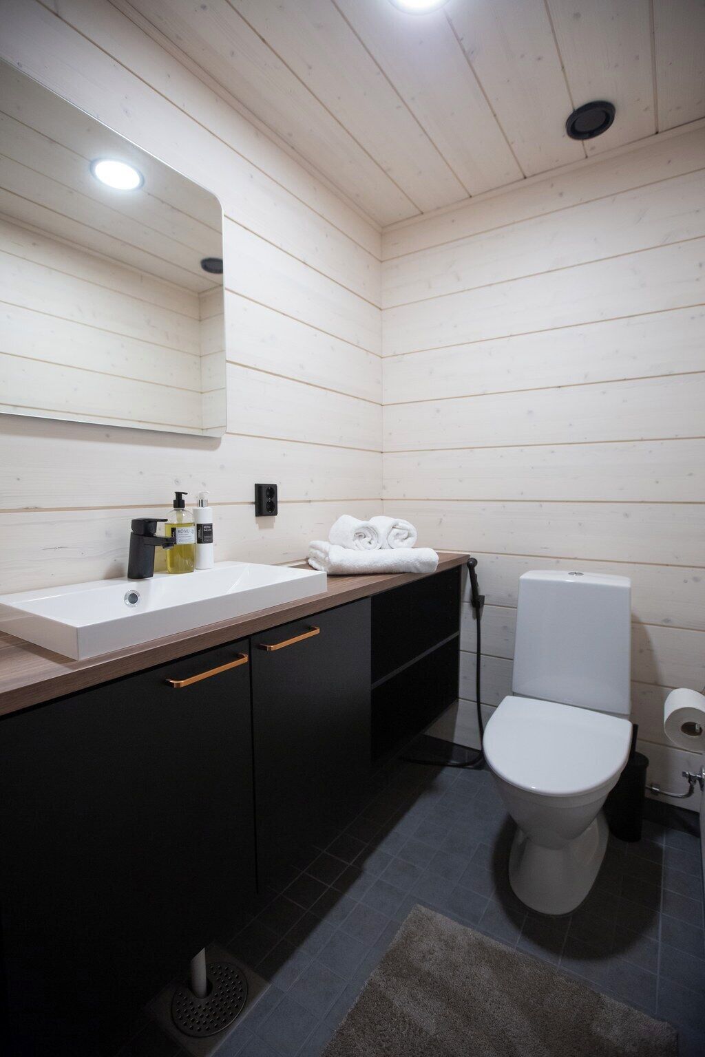 Ein modernes Badezimmer mit einem weißen Waschbecken, schwarzen Schränken, einer weißen Toilette und einem Spiegel über dem Waschbecken.