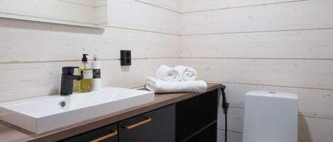 Ein modernes Badezimmer mit einem weißen Waschbecken, schwarzen Schränken, einer weißen Toilette und einem Spiegel über dem Waschbecken.