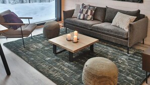 A modern living room with a large window, a hanging light fixture, a sofa with cushions, a coffee table, and a rug.