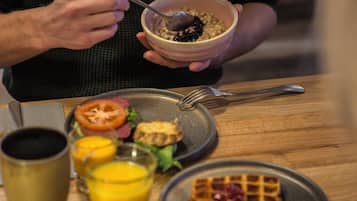 En frukostuppläggning med en skål med flingor, en tallrik med en grillad tomat, en våffla och en skål med sallad.