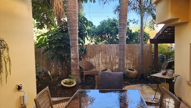A patio with a table and chairs, surrounded by a bamboo fence, palm trees, and a window. - Welcoming villa with AC in charming Herut with calm atmosphere and lot of space (Herut)