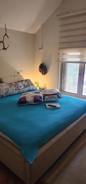 A bed with a blue cover, two pillows, a remote control, and a book on it. - Welcoming villa with AC in charming Herut with calm atmosphere and lot of space (Herut)