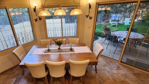A dining area with a wooden table, white chairs, and a view of a backyard through large windows. - Welcoming villa with AC in charming Herut with calm atmosphere and lot of space (Herut)