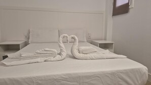 Une chambre d’hôtel avec un lit bien fait, deux tables de chevet et une fenêtre avec des stores.