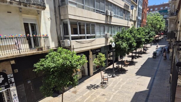Une rue bordée d’immeubles, d’arbres et de terrasses.