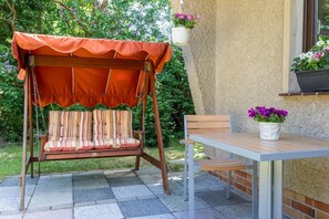 A patio with a swing chair, a table, and potted plants.